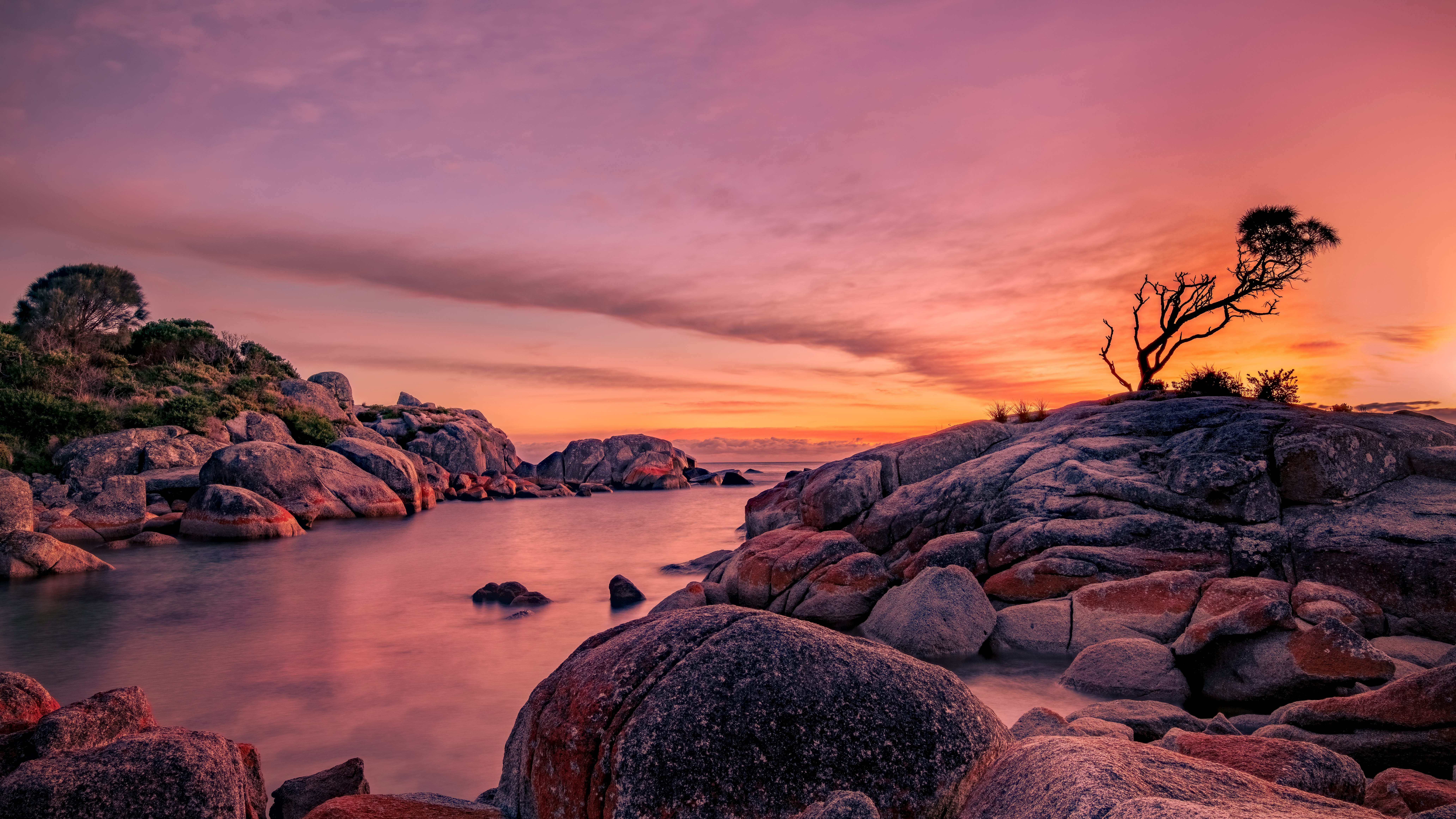 silhouette of person standing on rock formation near body of water during sunset